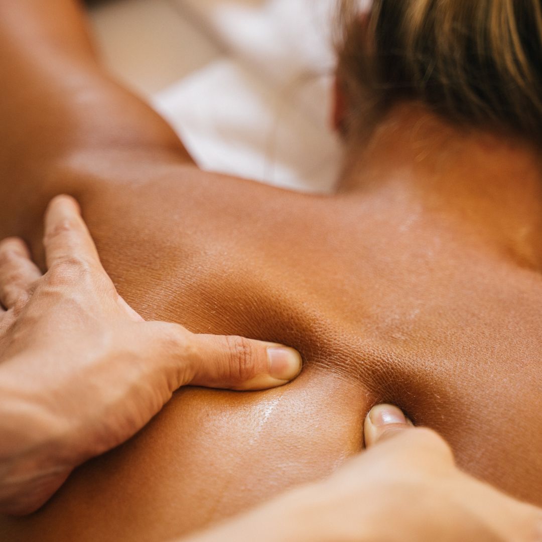 Close-up of a person receiving a massage, with a focus on the therapist's hands applying pressure to the back and shoulders